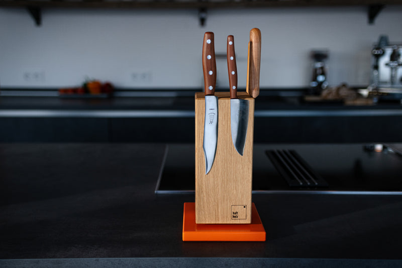 Im Vordergrund ein Messerhalter der magnetisch ist, an dem Block sind drei Küchenmesser geheftet. Im Hintergrund ist eine Küche zu sehen.