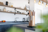 Eine Küche im Hintergrund mit einem Nussbaum Messerblock der im Fokus steht. Der Messerblock ist bestückt mit mehreren Küchenmessern